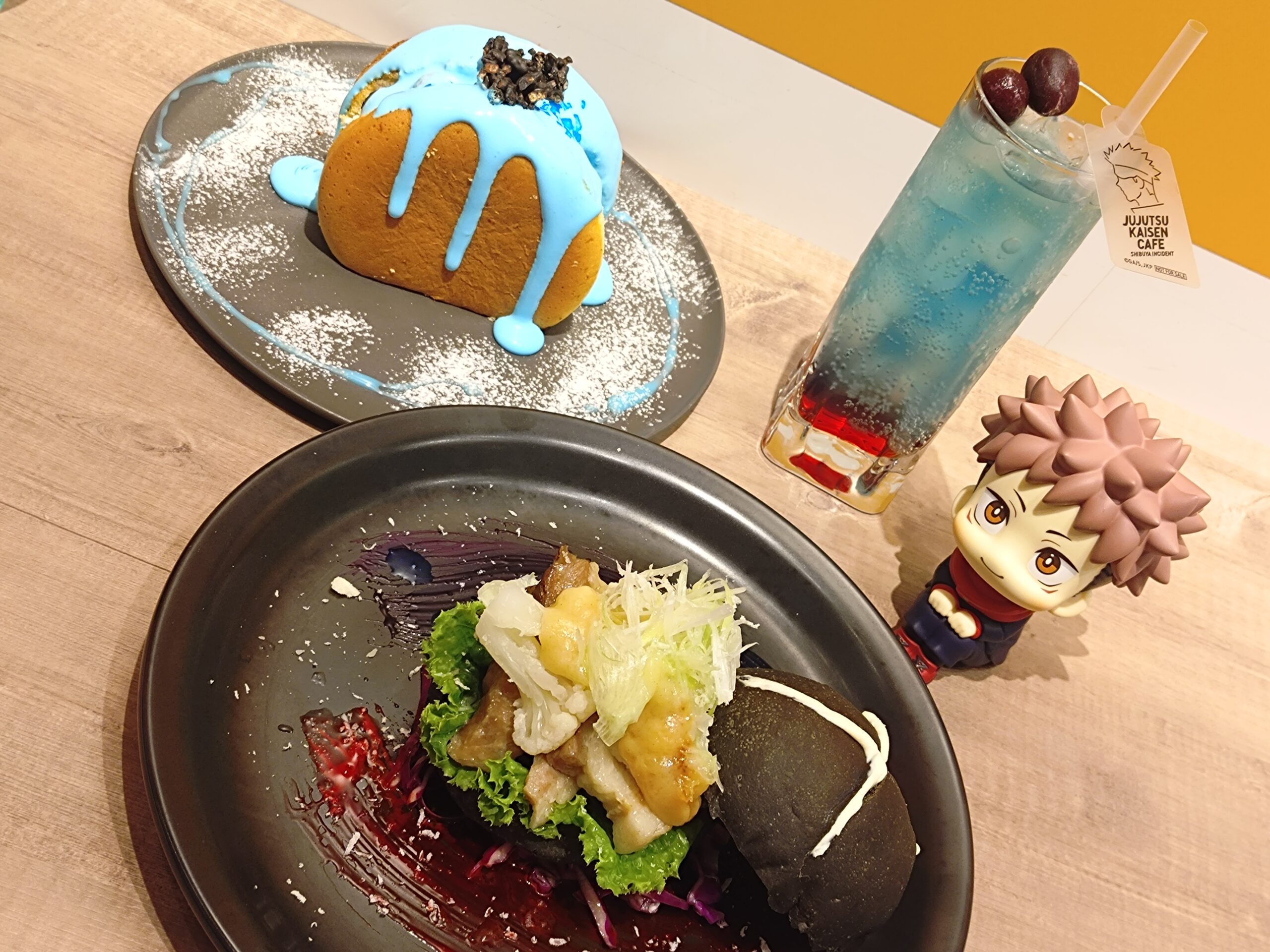 呪術廻戦カフェ2025渋谷事変の五条悟メニュー3種セット。西京『最強』味噌サンド、『無下限呪術』パンケーキ、ザクロ＆ライチドリンクを並べて撮影した写真。最強の術師・五条悟をテーマにしたフード、デザート、ドリンクが一緒に写っている。