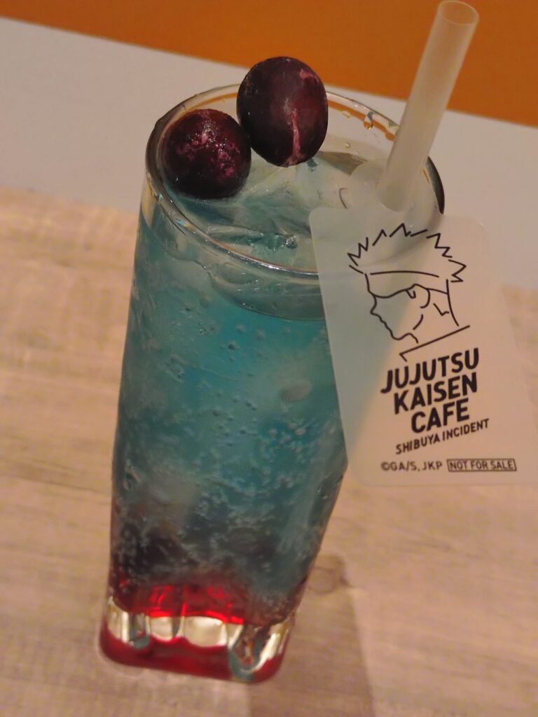 呪術廻戦カフェ2025渋谷事変の五条悟メニュー、ザクロ＆ライチドリンク。五条悟をイメージしたザクロとライチ風味の炭酸ソーダで、透明感ある見た目が特徴。