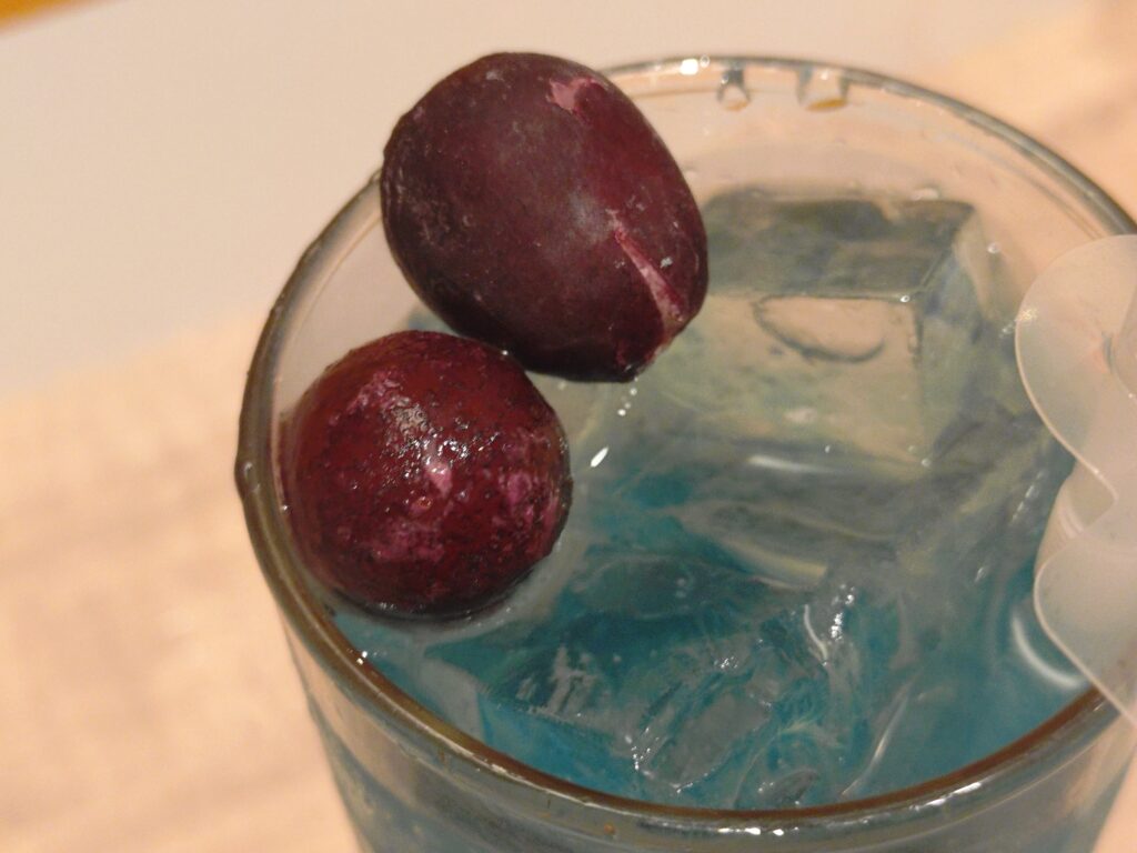 呪術廻戦カフェ2025渋谷事変の五条悟メニュー、ザクロ＆ライチドリンク。五条悟をイメージしたザクロとライチ風味の炭酸ソーダで、透明感ある見た目が特徴。