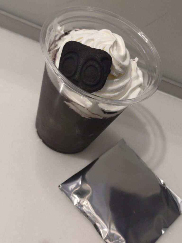 ミッドランドスクエアシネマの羅小黒戦記2コラボセットであるブラックココアドリンクと、ランダムでもらう開封前の缶ミラーを並べて撮影した写真。