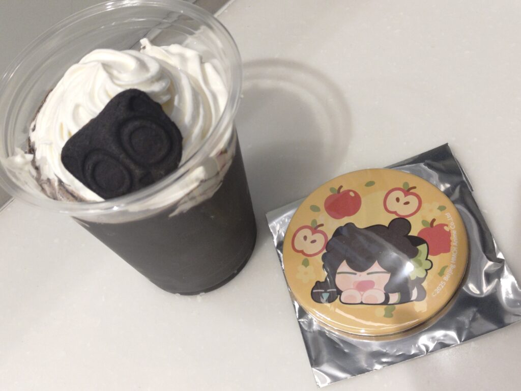 ミッドランドスクエアシネマの羅小黒戦記2コラボセットであるブラックココアドリンクと、シャオヘイ＆ヘイショの缶ミラーを並べて撮影した写真。